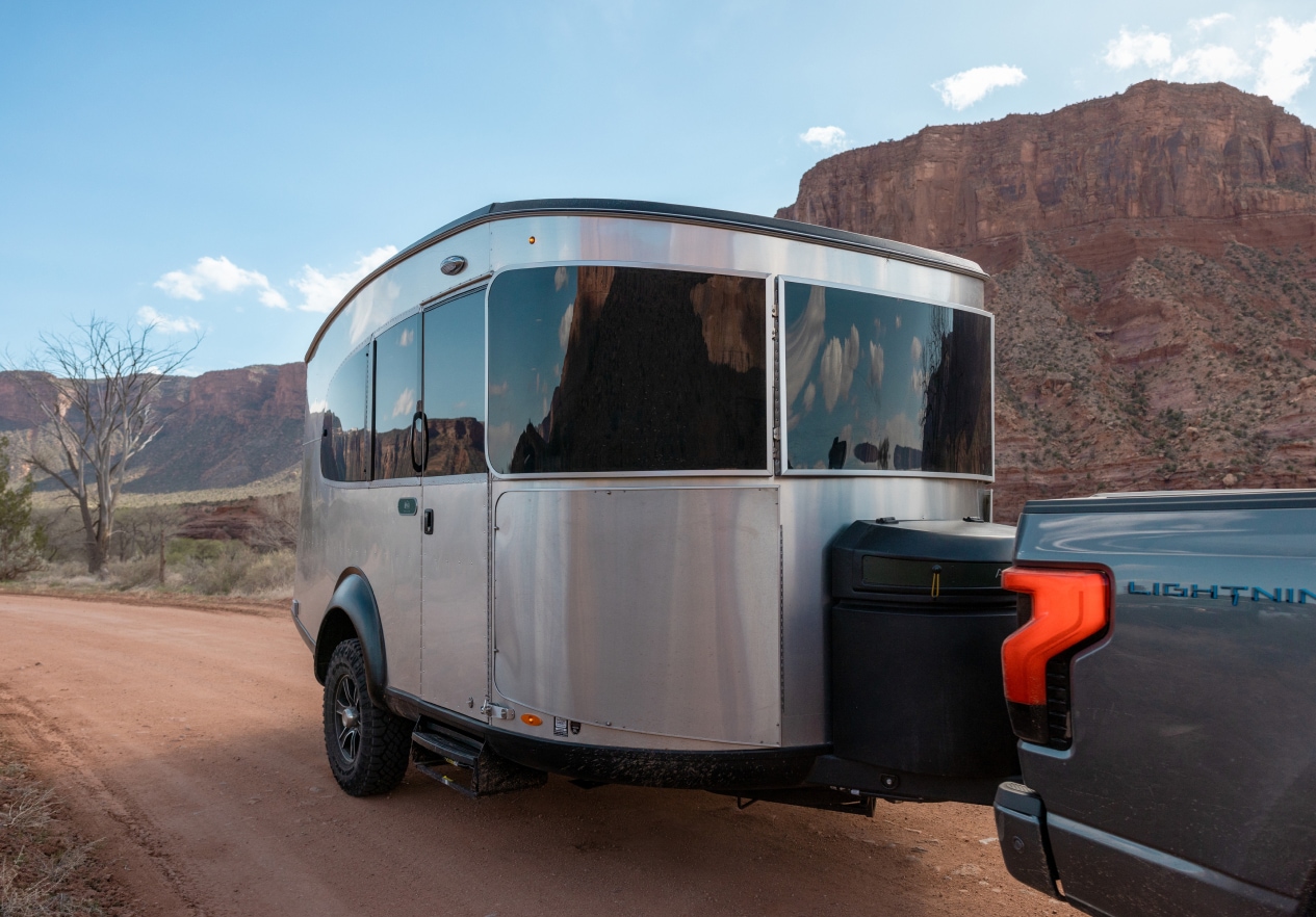 The R E I Co-op Special Edition Basecamp Trailer. A group of campers drink coffee outside their Airstream trailer.