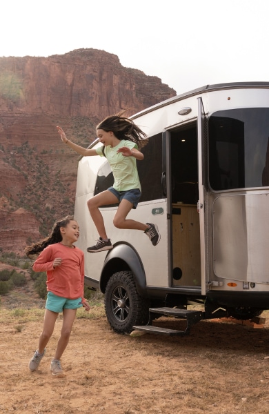 Two kids playing around an Airstream in a red desert landscape.