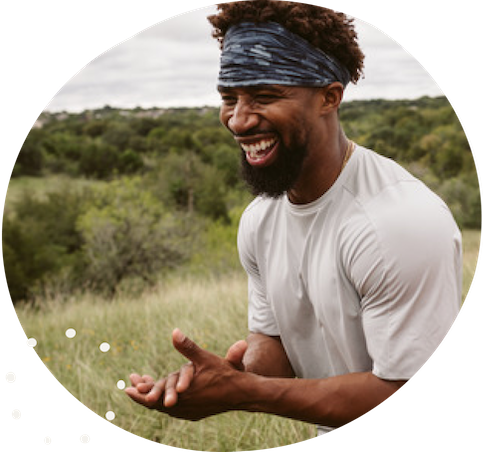 A smiling portrait of a black man clapping in a meadow.