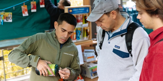 Mike Mojica, founder of Outdoor Element and a 2022 Navigate cohort participant, demonstrates his products to two customers at the Founders Market event outside the R E I Co-op Seattle flagship store.