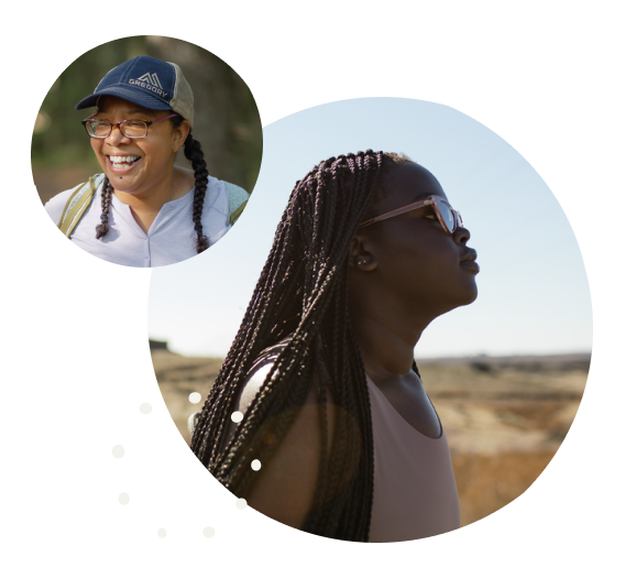 Two smiling women of color, adventuring outdoors and looking into the distance.