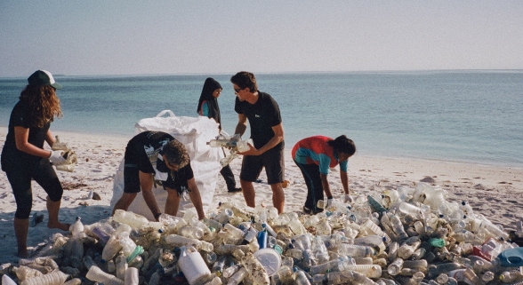 Volunteers collect discarded plastic on a beach.