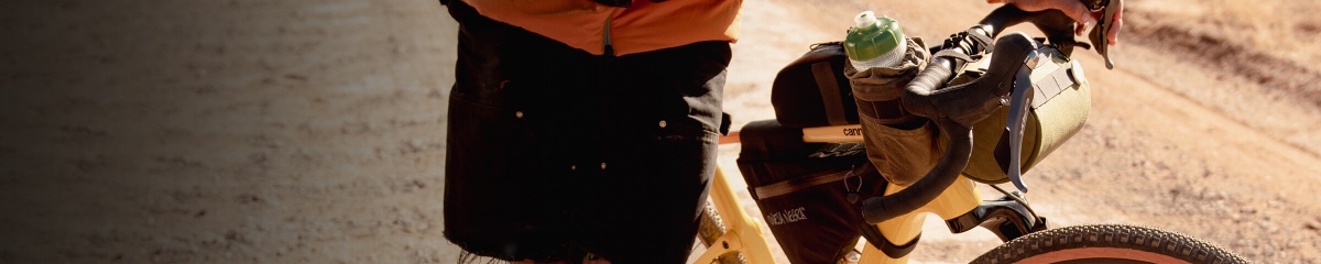 A super tight shot of a person standing next to their mountain bike. You can see various bags and baskets attached to the frame.