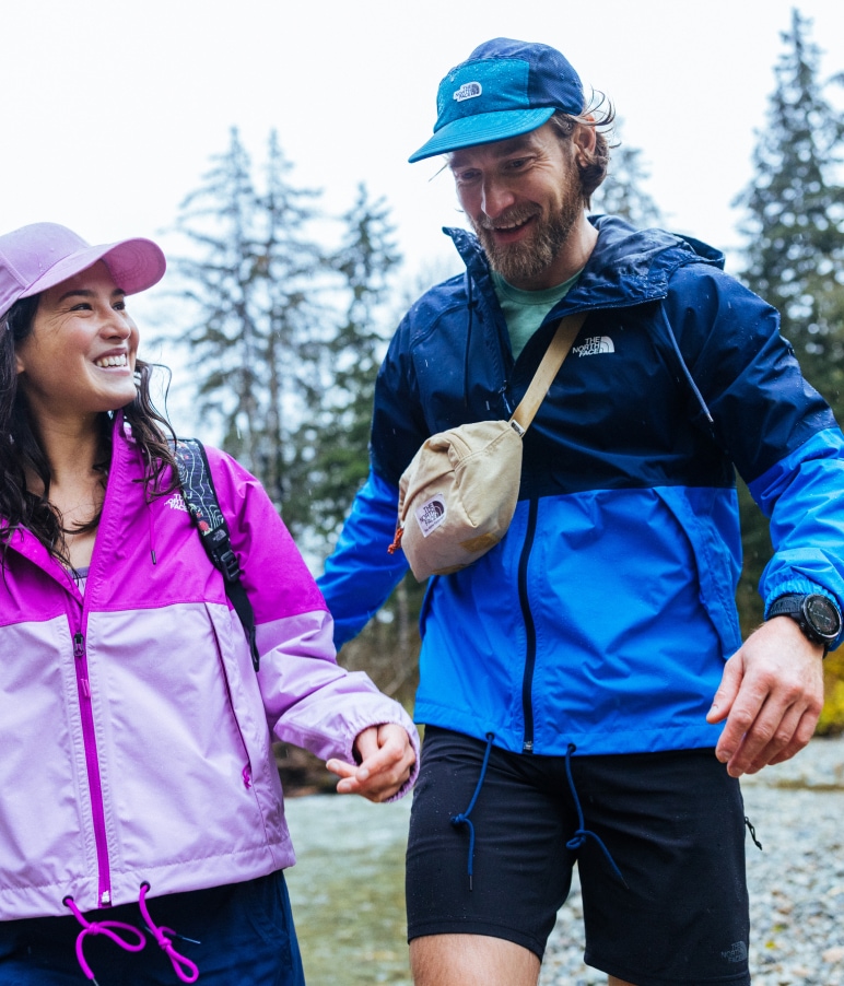 Two people smiling and wearing bright gear from The North Face, with towering trees in the background.