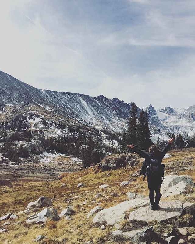 woman holding hands in the air on a mountain trail