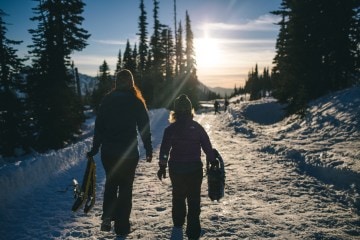 two women carrying snowshoes on a groomed winter trail