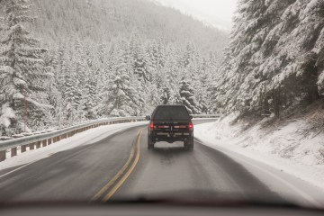 truck driving a winter road through snow covered trees