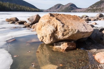 A rock in a body of shallow water in front of mountain peaks