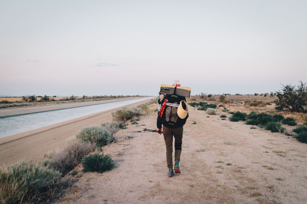 A single thru hiker with a large pack on walks through sand next to a road.