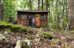 A cabin in the woods with a couple standing outside