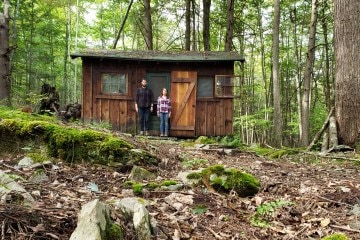 A cabin in the woods with a couple standing outside