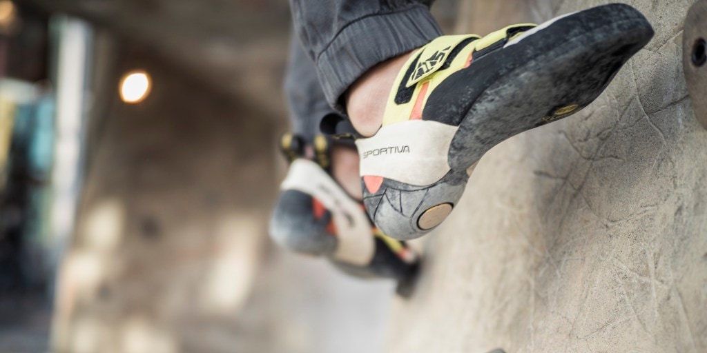 A climber carefully steps onto a small foothold in a climbing gym.