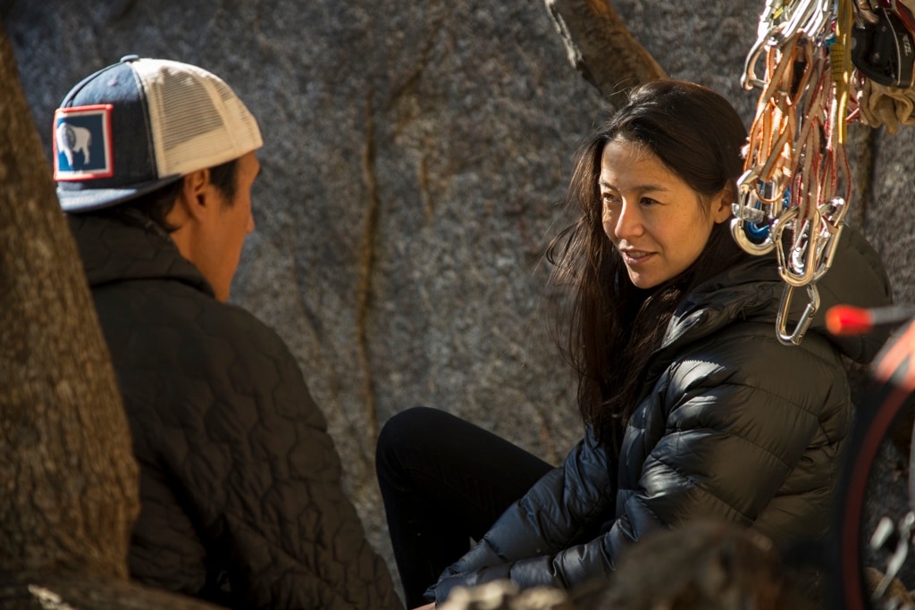 Jimmy Chin and Chai Vasarhelyi have a conversation amongst climbing gear, sitting against a cliff face.