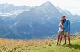 The couple hugs with a backdrop of tall, snow topped mountains.