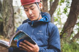 A rock climber wearing a helmet consults a guidebook at a crag.