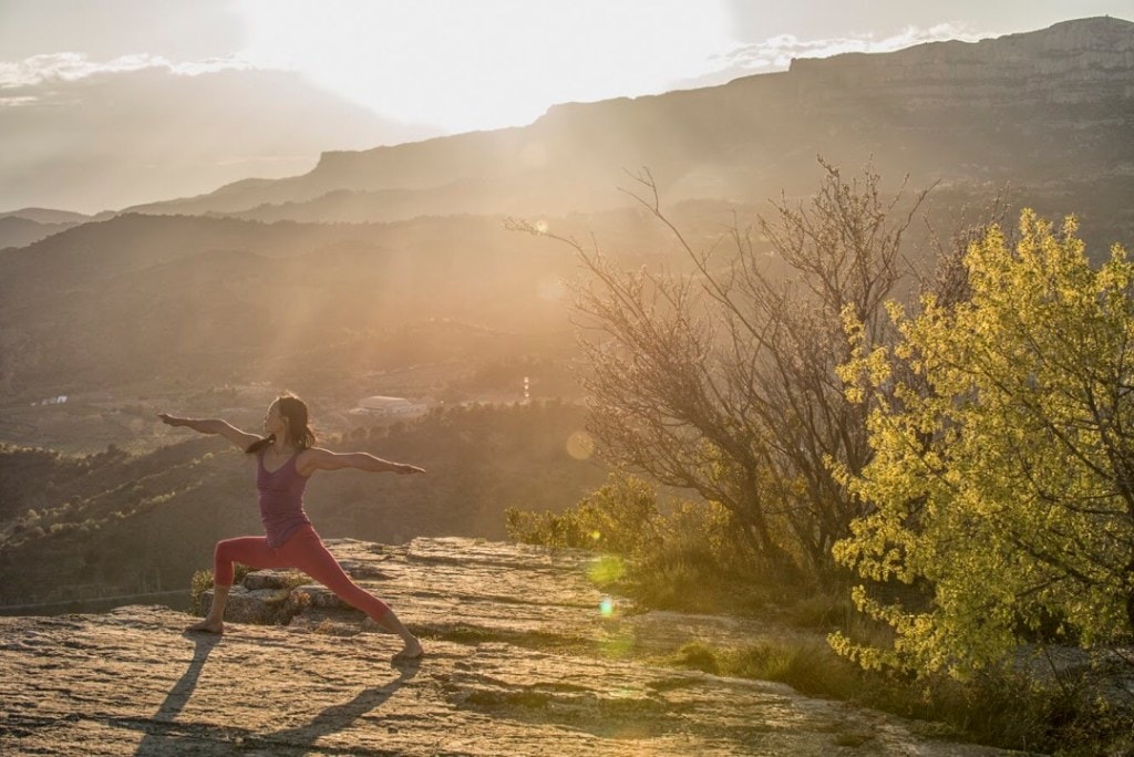 Olivia Hsu practices Warrior 2 pose in sunrise light on a rock overlook.