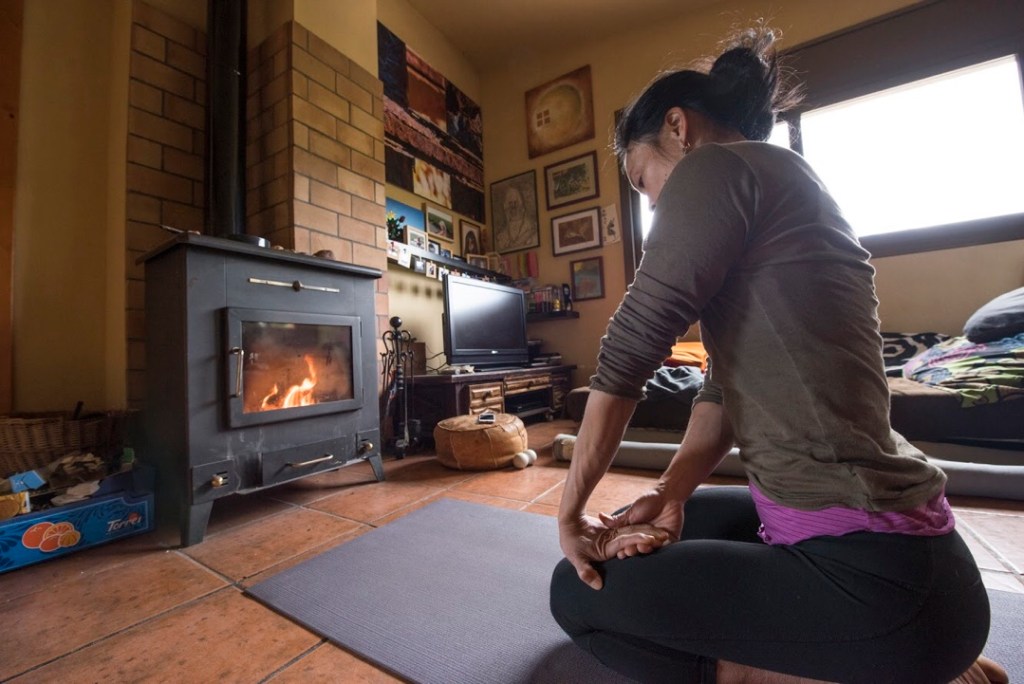 In front of a wood-burning stove, Olivia Hsu sits on a yoga mat, stretching her left forearm.