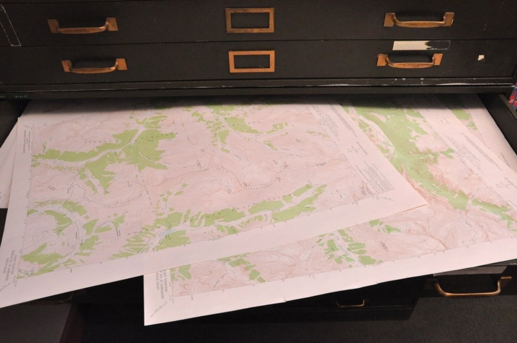 Green and white maps stick out from a wide, shallow drawer.