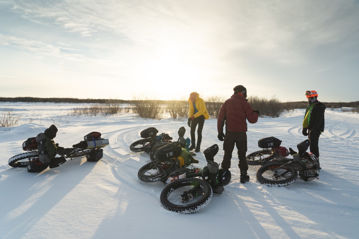 Three people and their bikes on a snowy field.