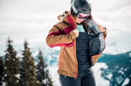 A skier zips up her jacket over a pair of bib pants.