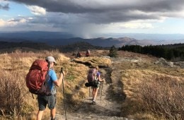 Hikers traverse a high-alpine field under stormy skies