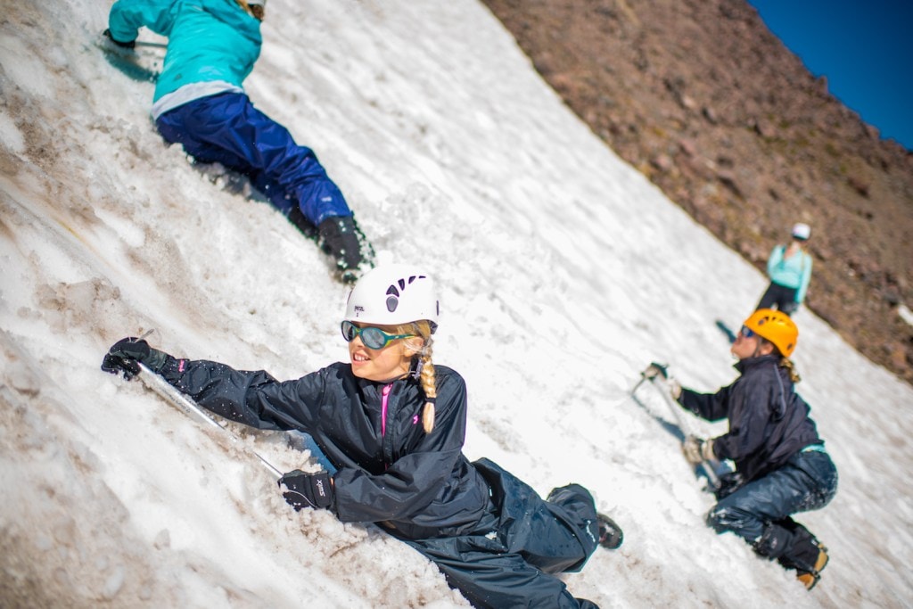 A young girl learns to use an ice ax to self arrest on snow. 