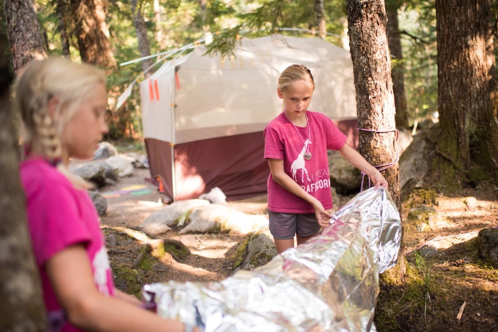 Two girls learn to build a shelter in the woods.