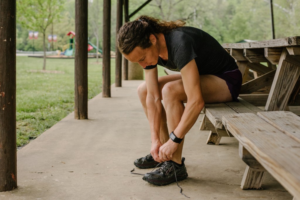 Grace Fisher sits on a bench while tying up her trail running shoes.