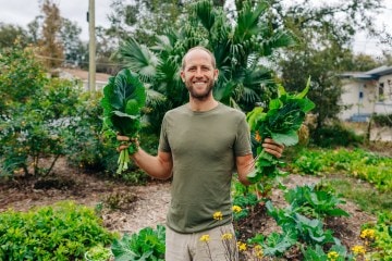 Rob Greenfield in a garden holding green leafy vegetables.