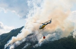 A helicopter is flying over a forest fire with a container of water beneath it.