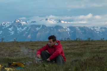 Brendan Leonard sitting down and eating in a field with mountains in the background.