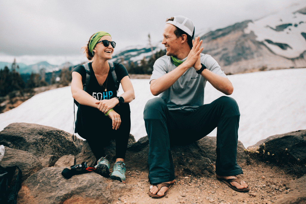 A woman and a man sit next to each other laughing near a snow field