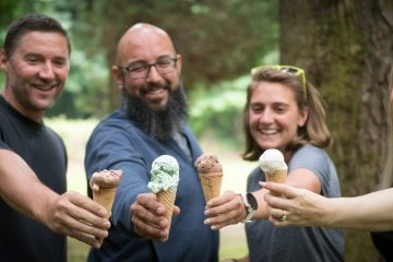 Four people smile and cheers their ice cream in cones.