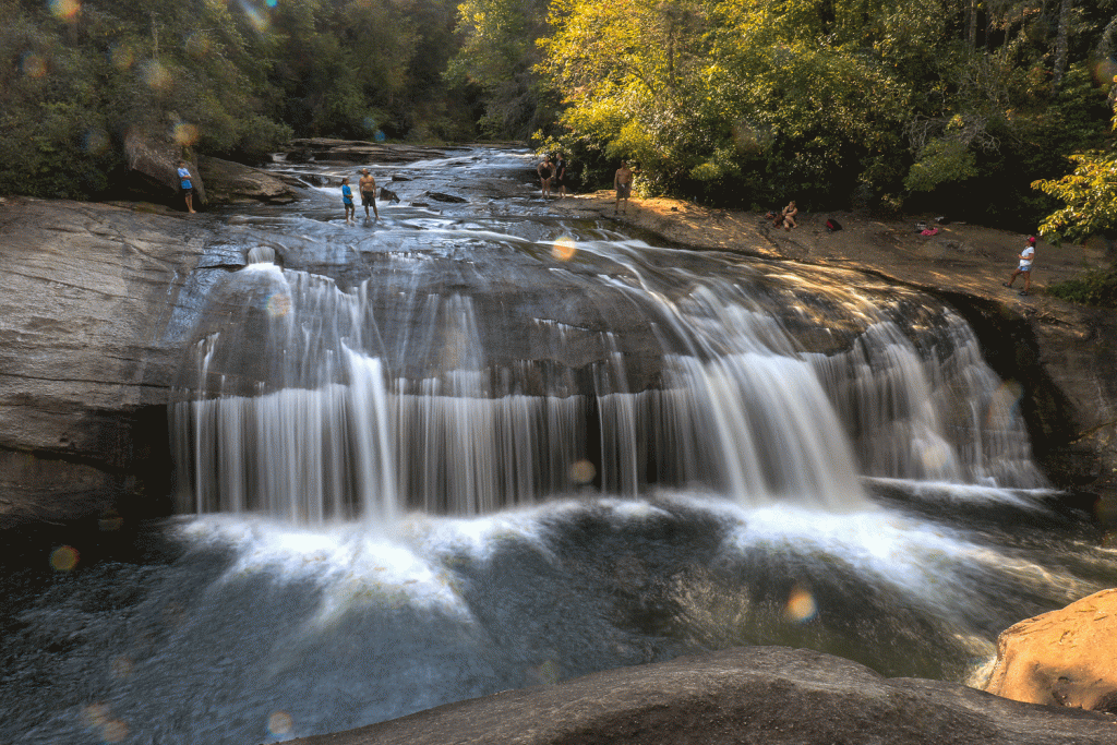 A rushing waterfall with swimmers standing at the top