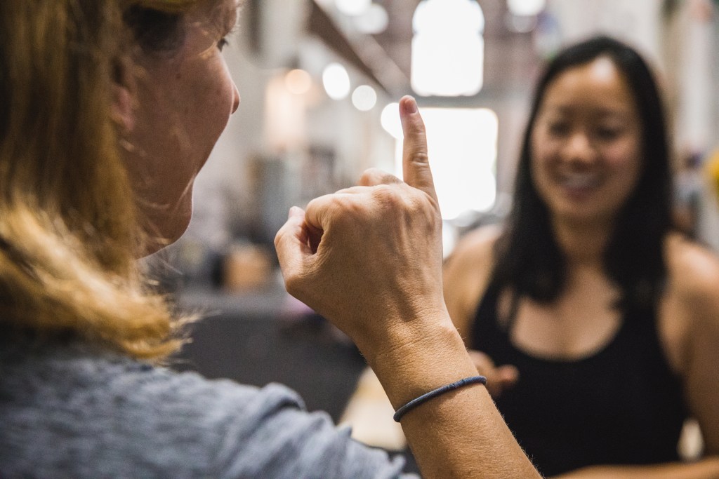 Close up photo of the back of a signing hand, a climber's face smiling in the background.