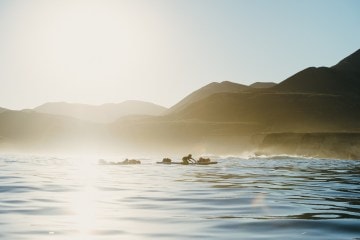 Two men paddling on stand up paddleboards with the sun setting behind them.