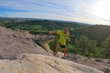 Joe Gray, wearing a green shirt and black shorts, is running up a rocky trail.