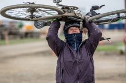 Kailey Kornhauser holding a bike over her head while smiling at the camera.