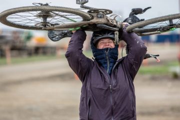 Kailey Kornhauser holding a bike over her head while smiling at the camera.