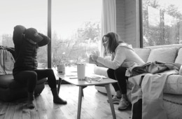 Two Arc'teryx designers are talking over a coffee table. One woman is pulling back her hair while the other woman holds a piece of fabric in her hand.