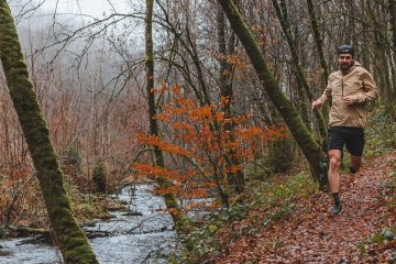 Karel Sabbe is running on a trail next to a river. There is fall foliage in the background and on the ground.