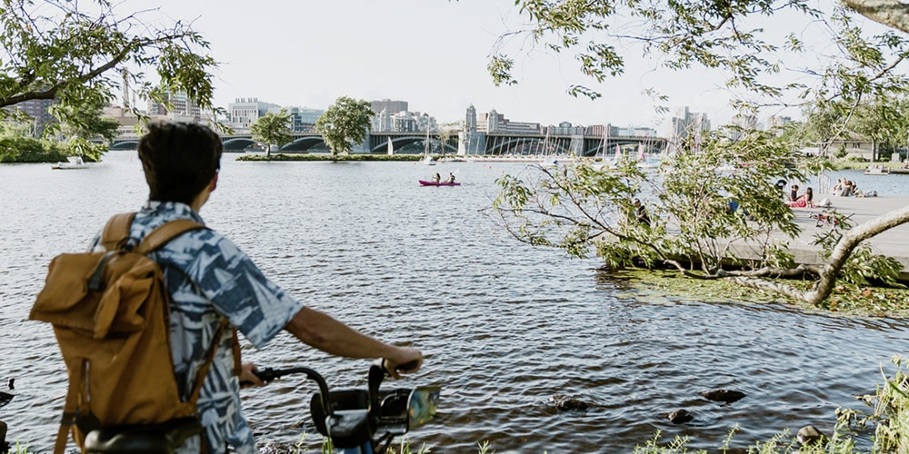 Person holding onto bike looking at lake with city skyline in distance.