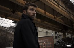 Brett Eldredge is standing underneath a bridge and looking over his shoulder at the camera.