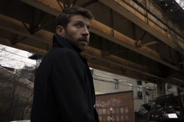 Brett Eldredge is standing underneath a bridge and looking over his shoulder at the camera.