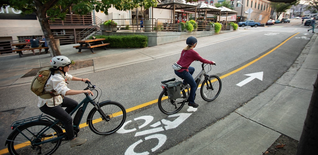 Two people riding electric bikes in a bike lane.