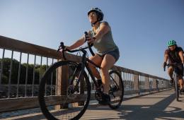 A person wearing shorts rides a bike along the person with another cyclist following.