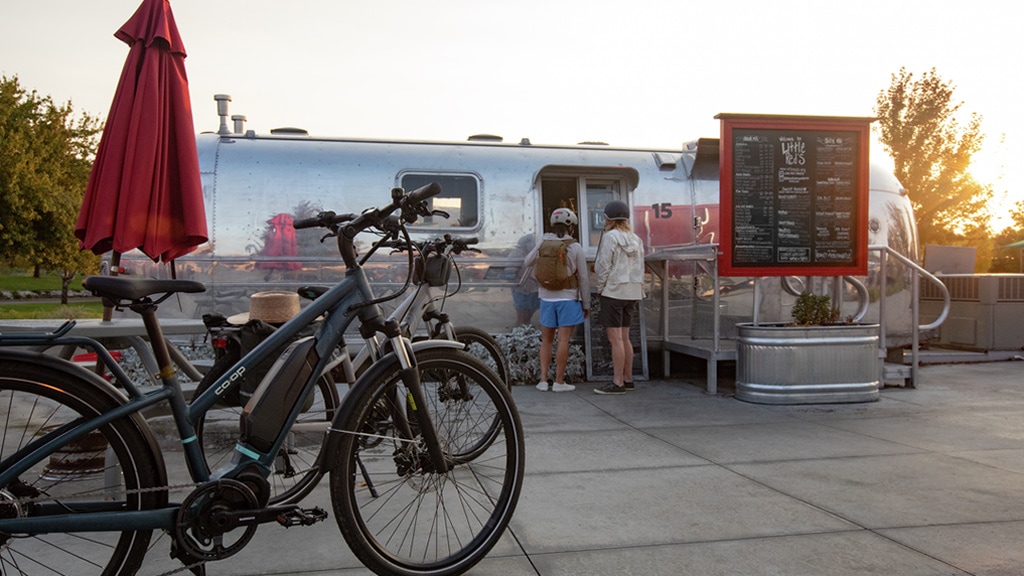 Two cyclists parked in front of food truck and buying a snack.