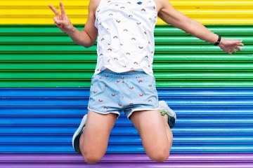 A runner jumps up into the air in front of a rainbow background