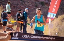 Allie McLoughlin, wearing a teal tank top is running on a dirt trail about to cross a finish line.