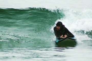 Adaptive athlete, Tim Brown, is on a surfboard catching a wave.